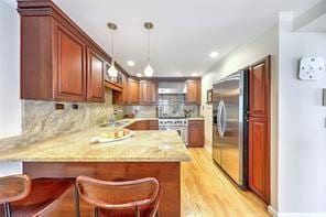 kitchen with light wood-style flooring, stainless steel refrigerator, decorative light fixtures, recessed lighting, and a peninsula