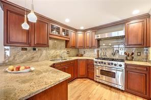 kitchen with light stone countertops, a sink, pendant lighting, high end stainless steel range, and wall chimney exhaust hood