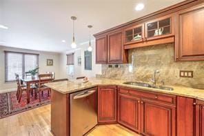 kitchen with a peninsula, a sink, hanging light fixtures, glass insert cabinets, and dishwasher