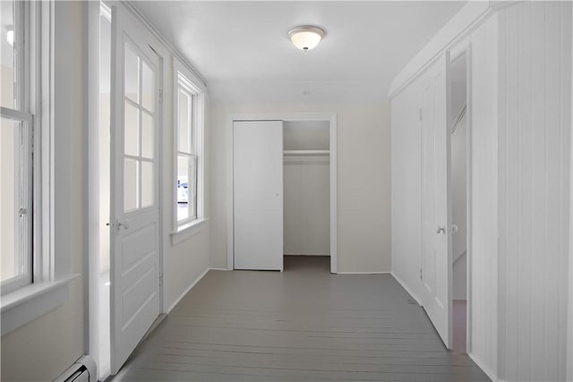 hallway featuring a baseboard heating unit, wood finished floors, and baseboards