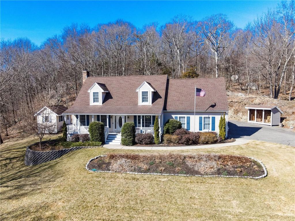 cape cod home with aphalt driveway, covered porch, a chimney, and a front lawn