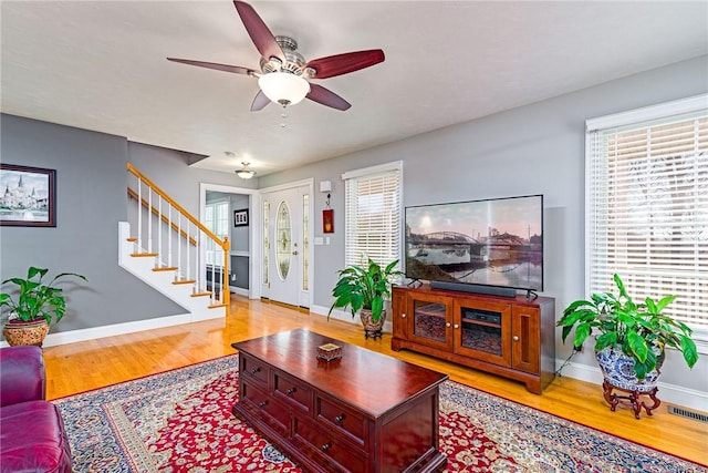 living room featuring visible vents, a ceiling fan, wood finished floors, baseboards, and stairs