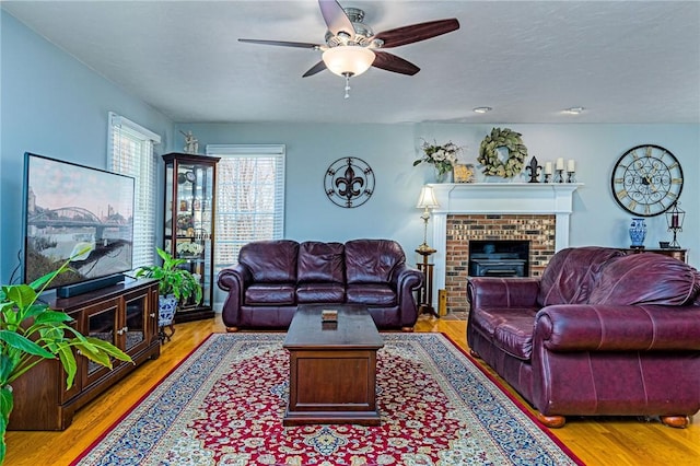 living area with a brick fireplace, a ceiling fan, and light wood-style floors