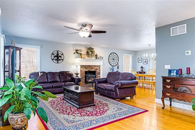 living room featuring light wood-style flooring, ceiling fan with notable chandelier, visible vents, and baseboards