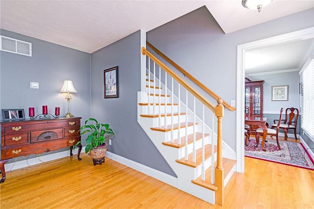 staircase featuring visible vents, ornamental molding, baseboards, and wood finished floors