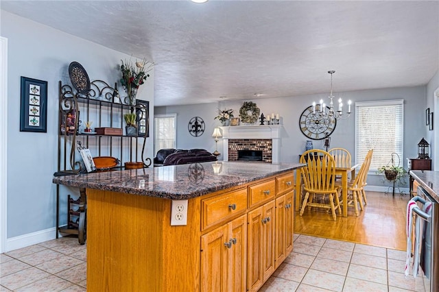 kitchen featuring a brick fireplace, a center island, open floor plan, dark stone counters, and light tile patterned floors