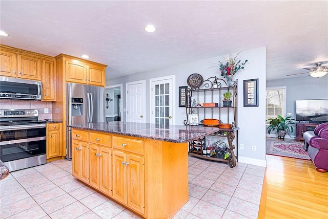 kitchen featuring dark stone countertops, light tile patterned floors, decorative backsplash, appliances with stainless steel finishes, and open floor plan