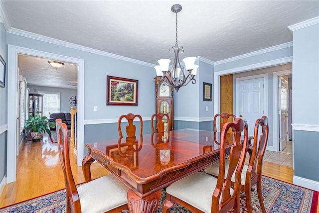 dining space with a textured ceiling, crown molding, light wood finished floors, and a chandelier