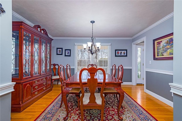 dining space with baseboards, an inviting chandelier, crown molding, and light wood finished floors