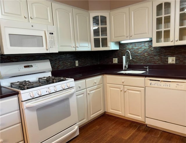 kitchen featuring dark countertops, a sink, backsplash, white appliances, and dark wood-style flooring