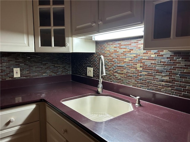 kitchen featuring a sink, glass insert cabinets, tasteful backsplash, and dark countertops