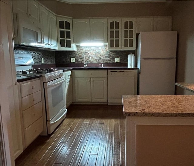 kitchen featuring glass insert cabinets, dark wood-type flooring, decorative backsplash, white appliances, and a sink