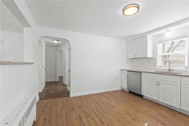 kitchen with radiator heating unit, arched walkways, a sink, white cabinets, and stainless steel dishwasher