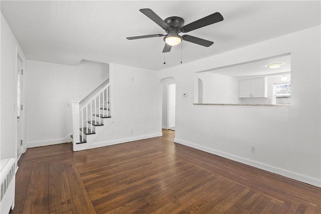 unfurnished living room featuring arched walkways, radiator, stairs, and baseboards