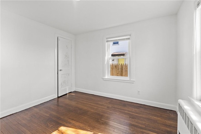 spare room featuring dark wood-type flooring, radiator, and baseboards