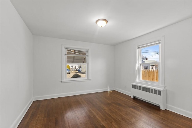 spare room with baseboards, dark wood-type flooring, and radiator