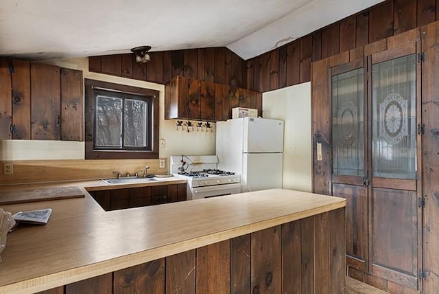 kitchen with white appliances, wooden walls, a peninsula, a sink, and vaulted ceiling