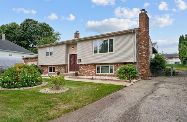 bi-level home with a front lawn, fence, brick siding, and a chimney