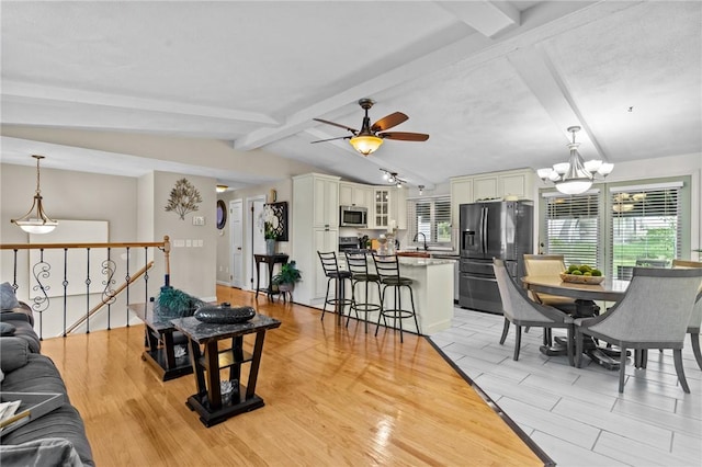 living area featuring light wood-style flooring, ceiling fan with notable chandelier, and lofted ceiling with beams