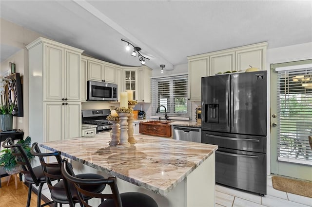 kitchen featuring light stone counters, a sink, cream cabinets, appliances with stainless steel finishes, and a breakfast bar area