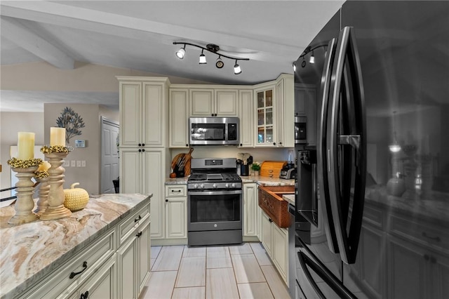 kitchen featuring light stone countertops, lofted ceiling with beams, glass insert cabinets, appliances with stainless steel finishes, and cream cabinets