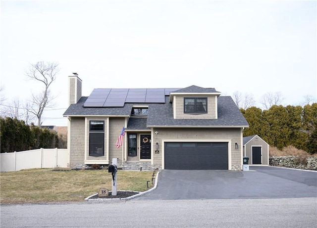 view of front facade featuring a front yard, fence, an attached garage, aphalt driveway, and roof mounted solar panels