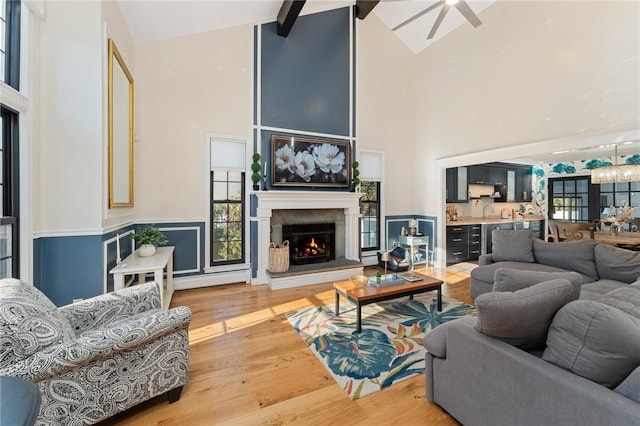 living area featuring high vaulted ceiling, plenty of natural light, wood finished floors, and a lit fireplace