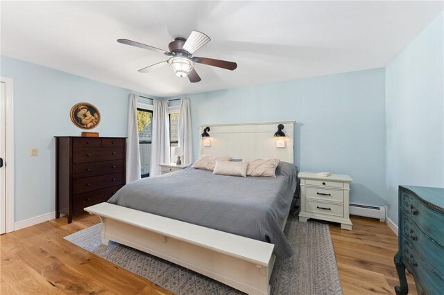 bedroom featuring ceiling fan, a baseboard heating unit, baseboards, and light wood-style flooring