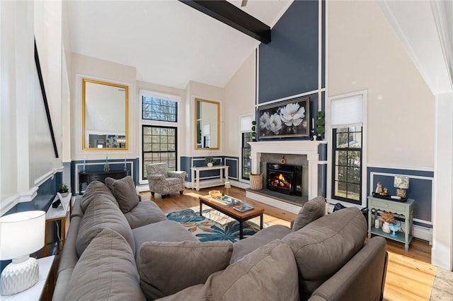 living room with beamed ceiling, wood finished floors, a warm lit fireplace, and high vaulted ceiling