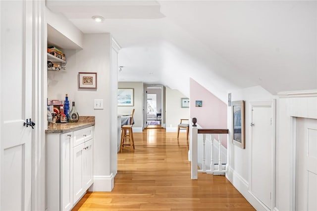 hallway with baseboards, an upstairs landing, vaulted ceiling, and light wood-type flooring