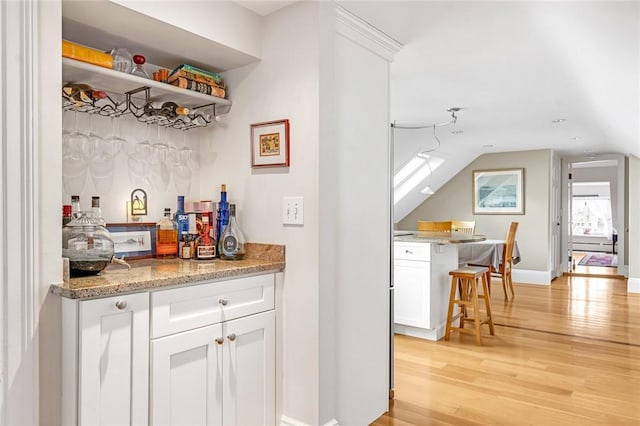 bar with a bar, light wood-style flooring, baseboards, and lofted ceiling