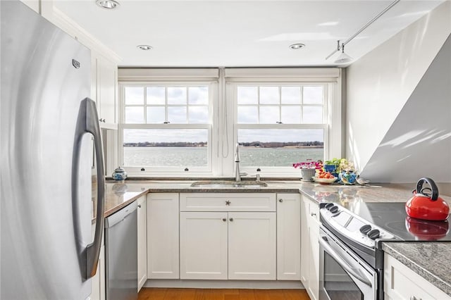 kitchen featuring a water view, stainless steel appliances, white cabinetry, a sink, and stone countertops