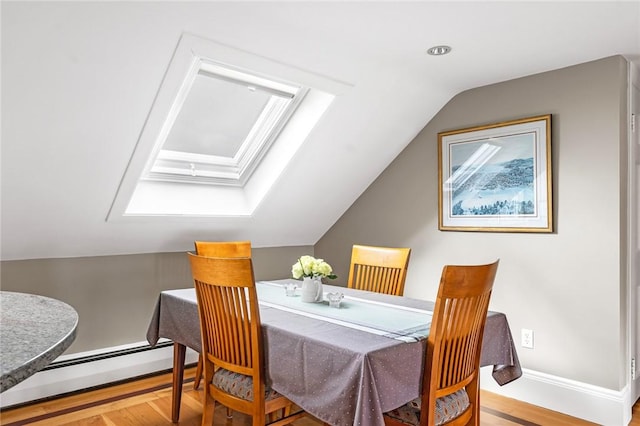 dining area featuring a baseboard radiator, vaulted ceiling with skylight, wood finished floors, and baseboards