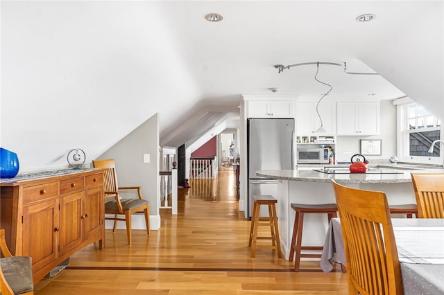 kitchen featuring a kitchen breakfast bar, white cabinetry, freestanding refrigerator, light wood-style flooring, and white microwave