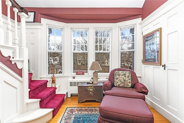 sitting room with stairs, wood finished floors, and radiator
