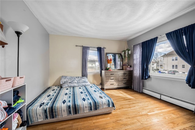 bedroom featuring multiple windows, baseboard heating, and wood finished floors