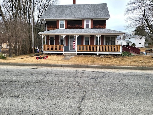 country-style home with a porch, roof with shingles, and a chimney