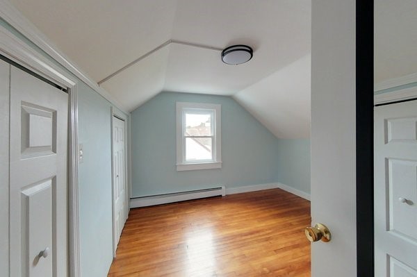 additional living space with a baseboard heating unit, lofted ceiling, and light wood-style floors