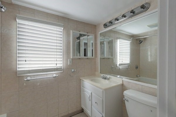 full bathroom featuring tiled shower / bath combo, toilet, tile walls, and vanity