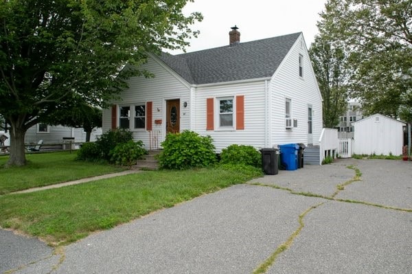 view of front facade with a front yard, cooling unit, driveway, roof with shingles, and a chimney