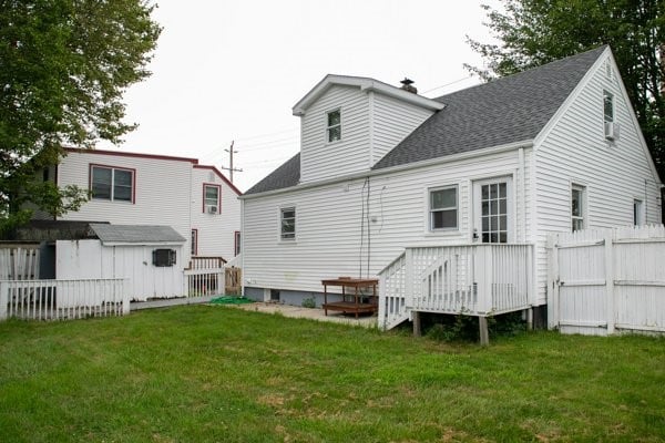 back of property featuring fence, roof with shingles, an outdoor structure, a yard, and a storage unit