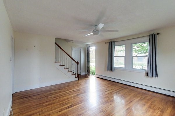 unfurnished room with baseboard heating, stairway, a ceiling fan, and wood finished floors