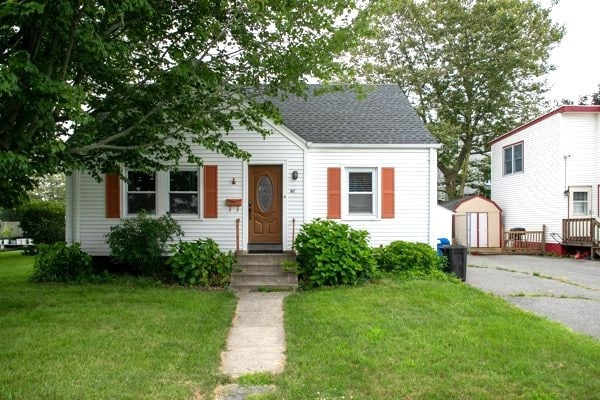 bungalow featuring an outbuilding, a storage unit, a front lawn, and a shingled roof