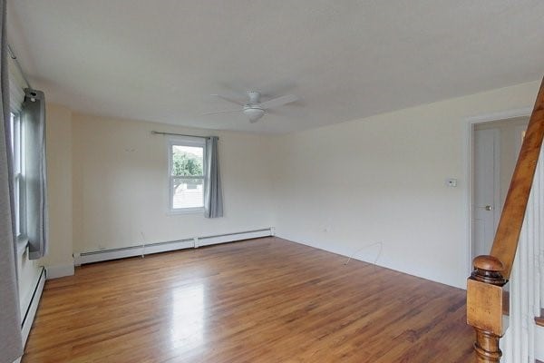 spare room featuring a baseboard heating unit, wood finished floors, a ceiling fan, and stairway