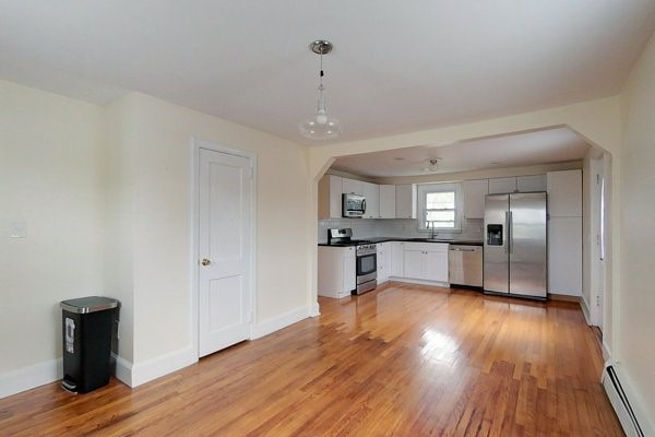 kitchen with stainless steel appliances, arched walkways, light wood-style floors, baseboards, and baseboard heating