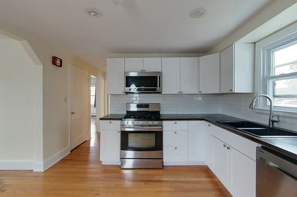 kitchen featuring a sink, tasteful backsplash, dark countertops, stainless steel appliances, and light wood finished floors