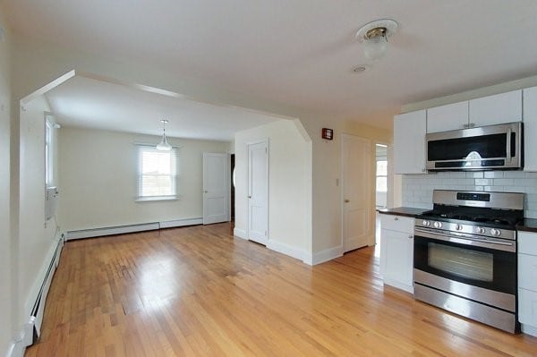 kitchen with light wood-type flooring, dark countertops, backsplash, appliances with stainless steel finishes, and a baseboard radiator