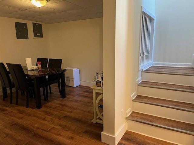 dining room with electric panel, wood finished floors, stairway, a paneled ceiling, and baseboards