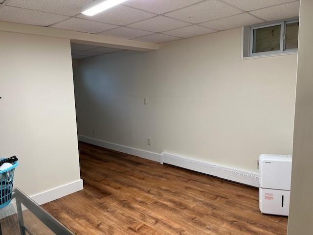 interior space featuring a drop ceiling, a baseboard heating unit, baseboards, and wood finished floors