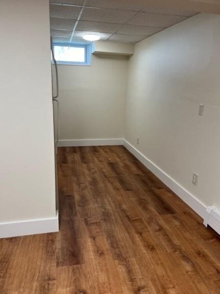 basement with a baseboard heating unit, a paneled ceiling, baseboards, and wood finished floors